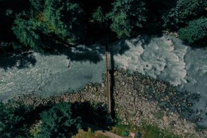 Stunning aerial shot of a wooden bridge spanning a rocky river surrounded by dense forest.